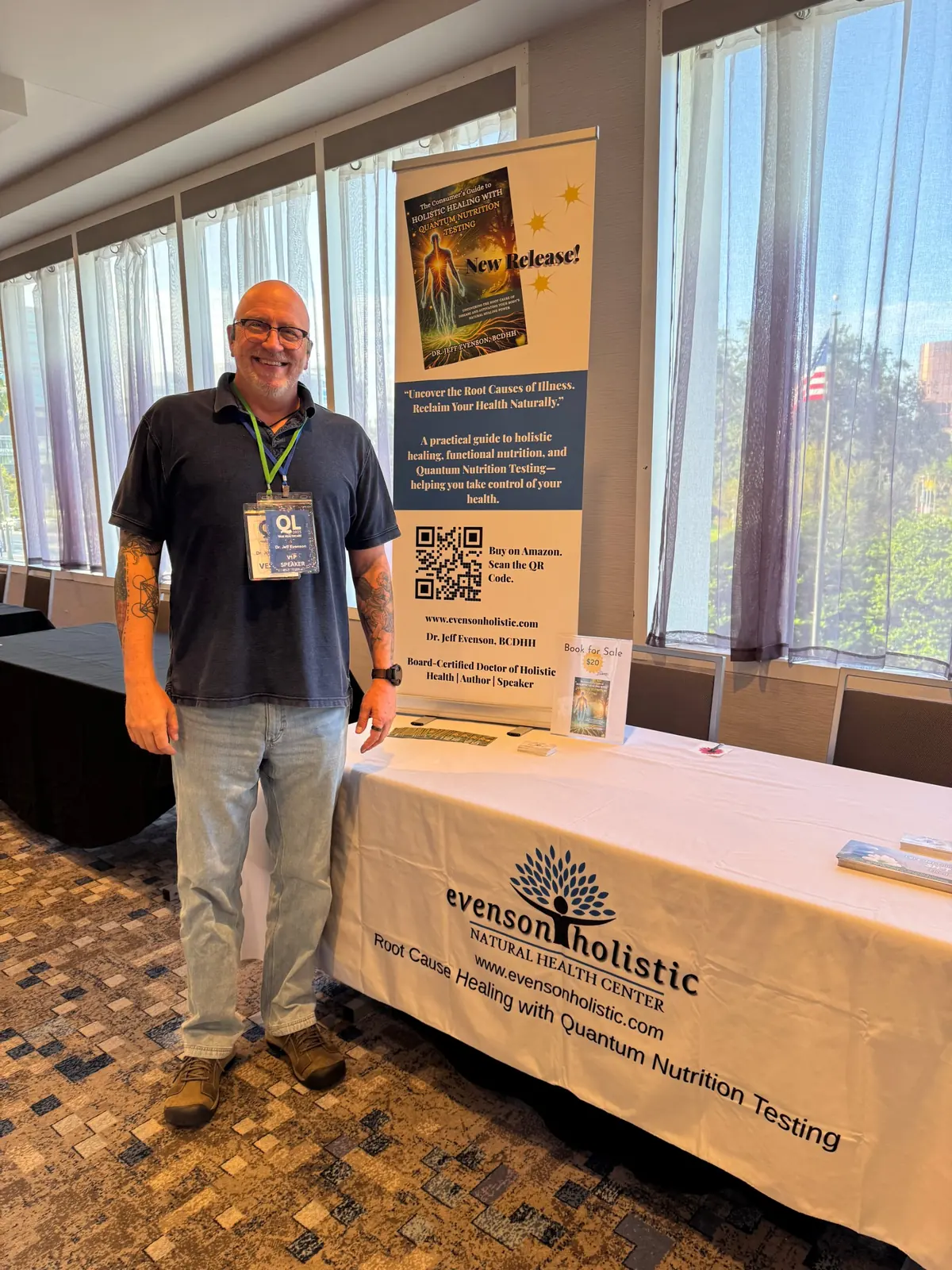 Jeff standing beside his book banner and practice table at a conference