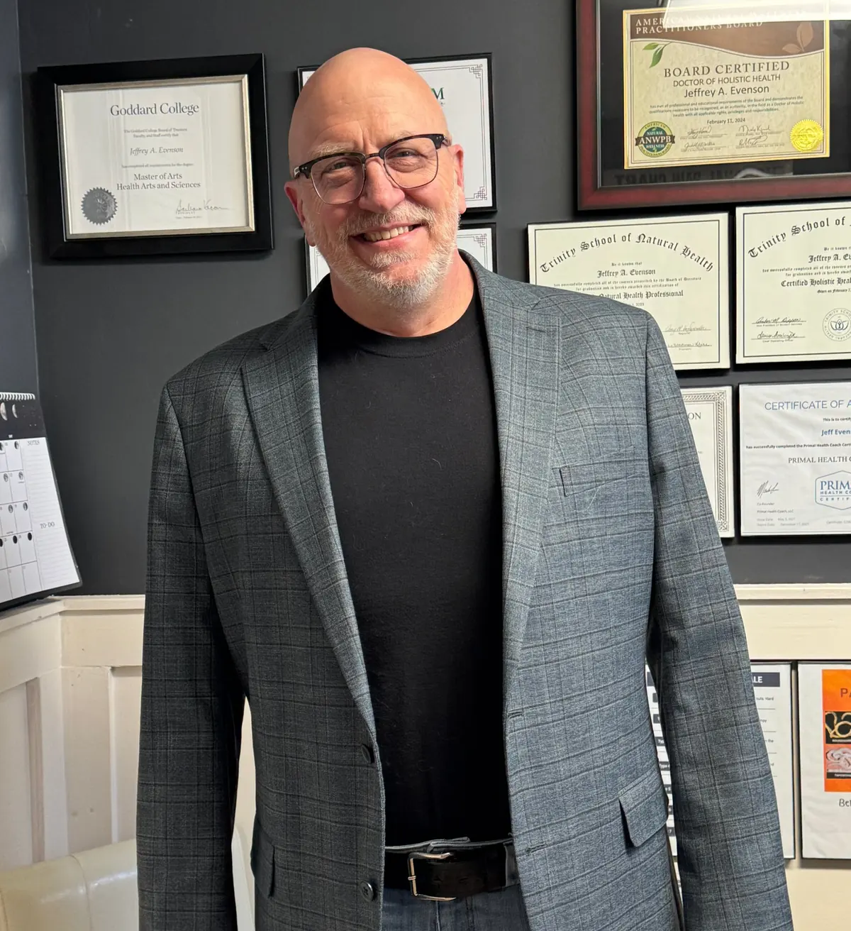 Jeff smiling in his session room in front of his framed degrees and certifications