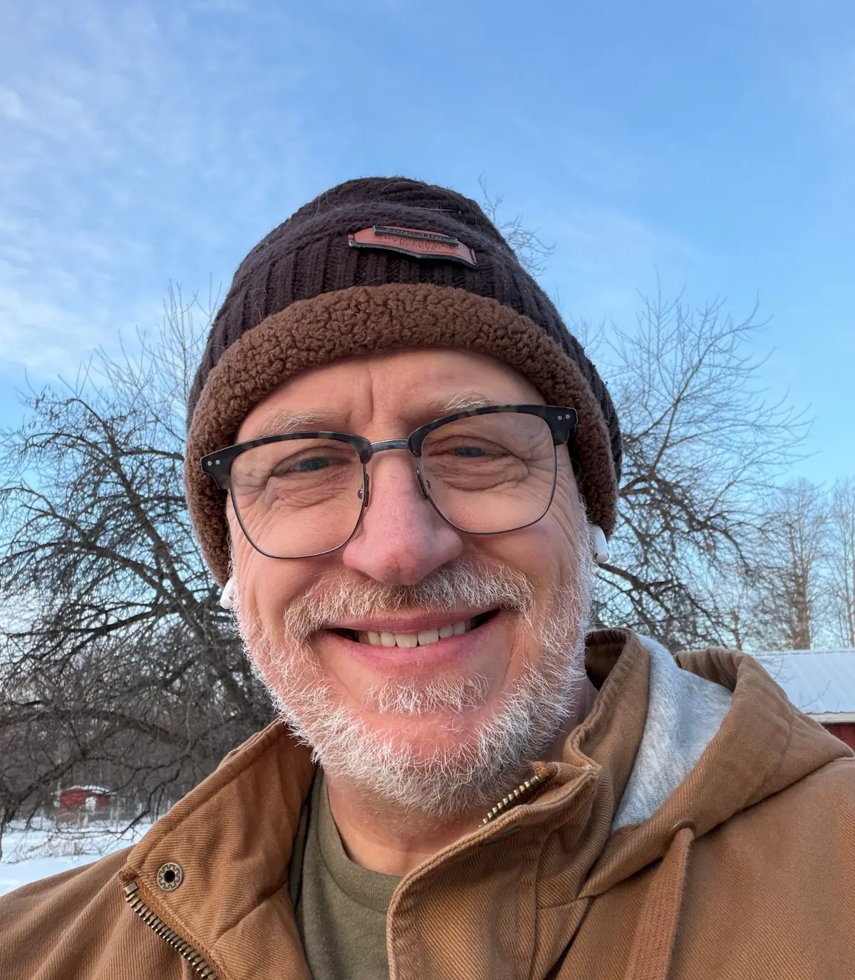 Jeff smiling outdoors in a knit cap and canvas work jacket, bare winter trees behind him